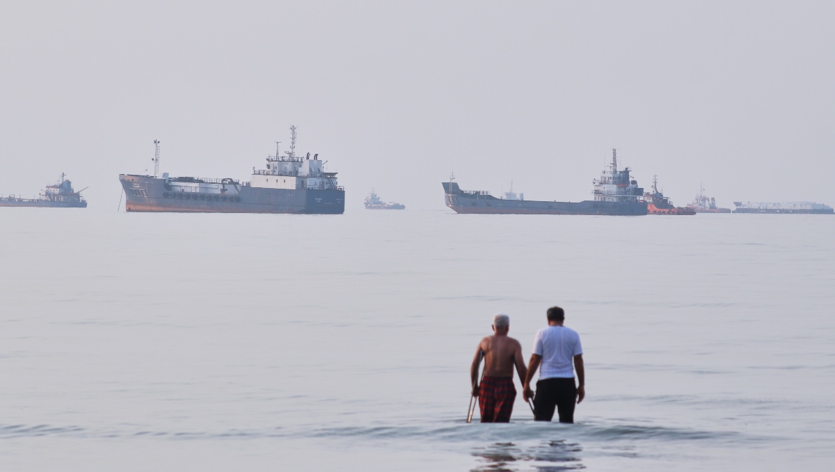 Dos hombres caminan en las aguas del estrecho de Ormuz con barcos fondeados más lejos, cerca de Bandar Abbas, Irán. | AP