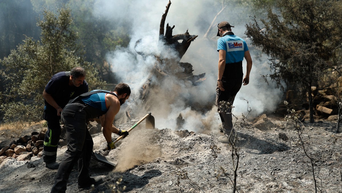 Residentes sofocan las brasas con tierra para evitar que se reavive el fuego tras lograrse controlar un incendio forestal cerca de La Adrada. | AFP
