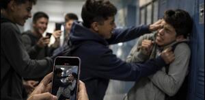 Imagen ilustrativa de una agresión entre estudiantes mientras otras personas la graban con un teléfono celular, una representación del happy slapping
