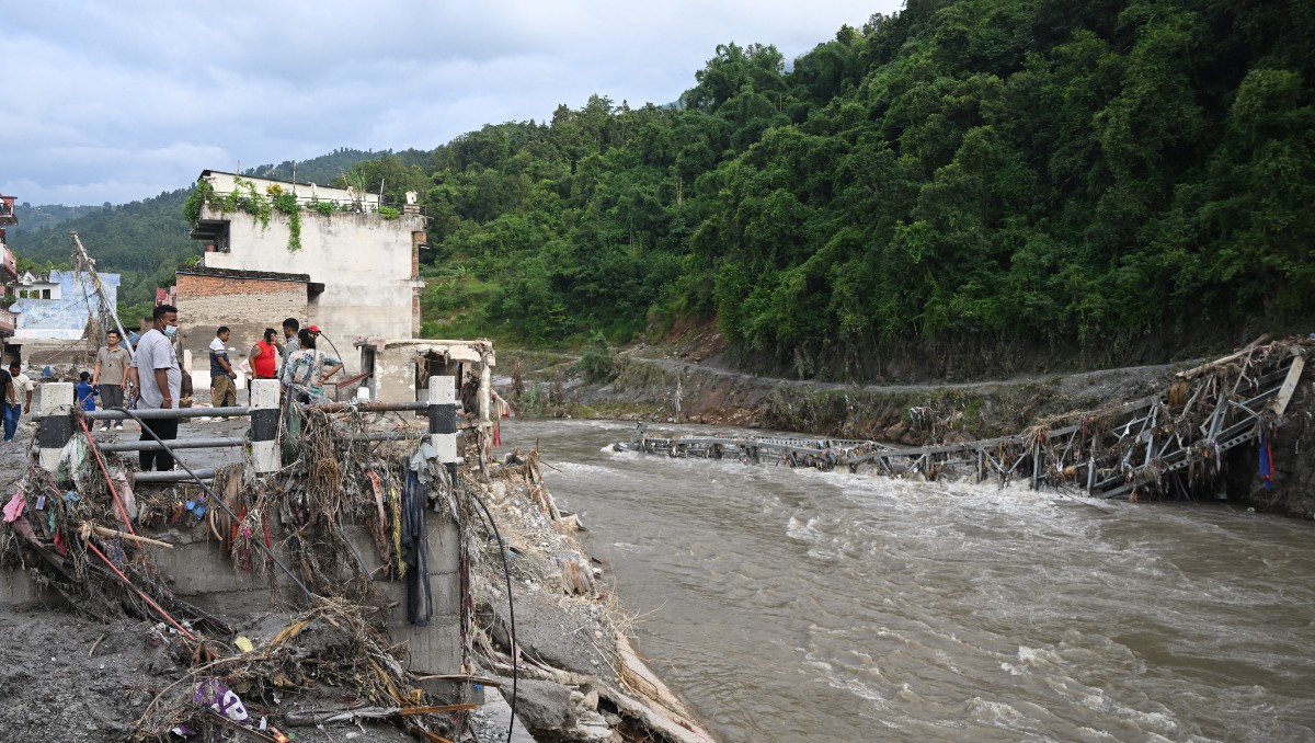 Personas permanecen de pie cerca de un puente derrumbado tras inundaciones en Devighat, distrito de Nuwakot | Foto: AFP