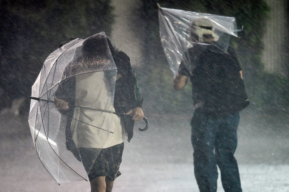 Los peatones se aferran a sus paraguas en medio de fuertes vientos y lluvias torrenciales en Chiba. | AFP