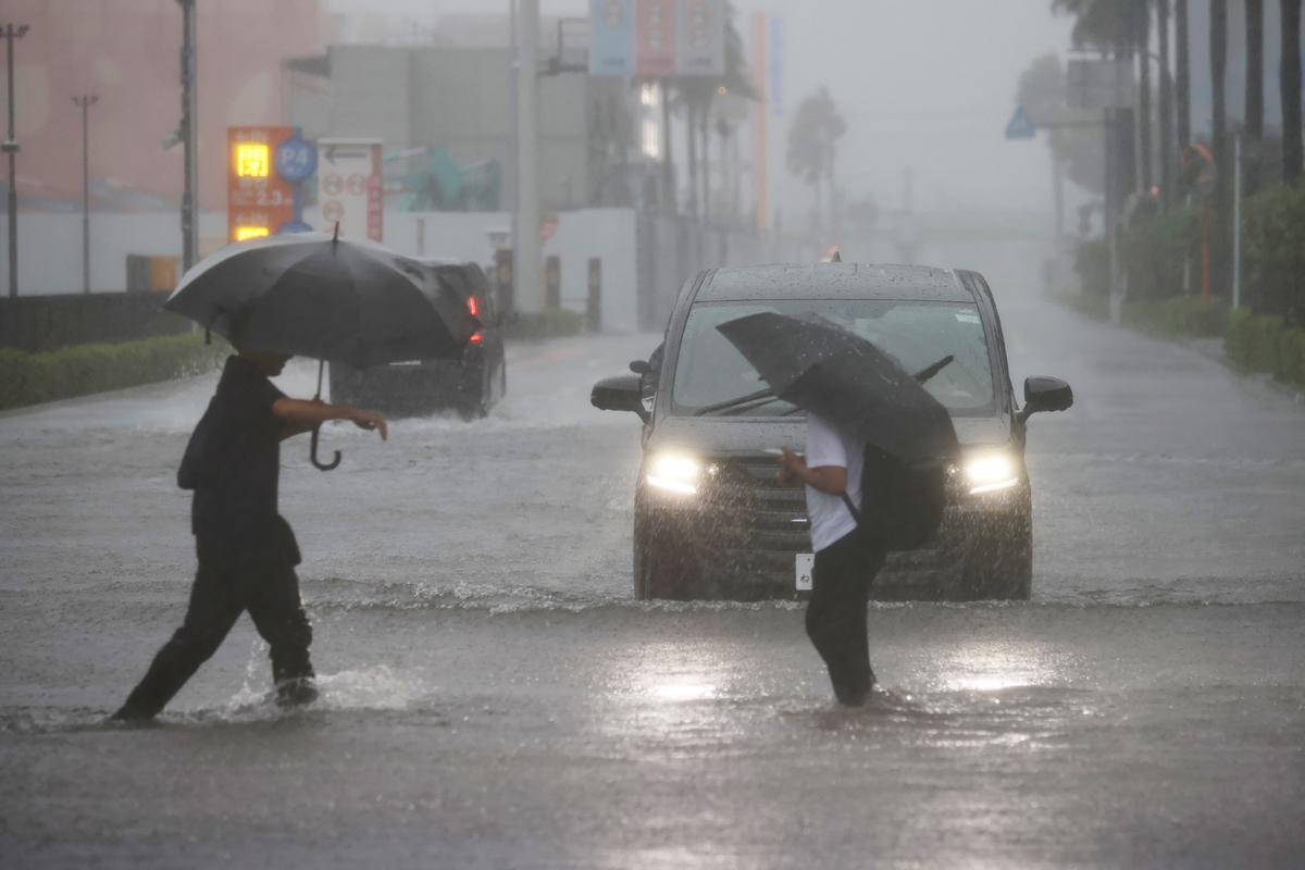 Varias personas caminan vadeando una carretera inundada mientras cae una lluvia torrencial debido a las condiciones meteorológicas. | AFP