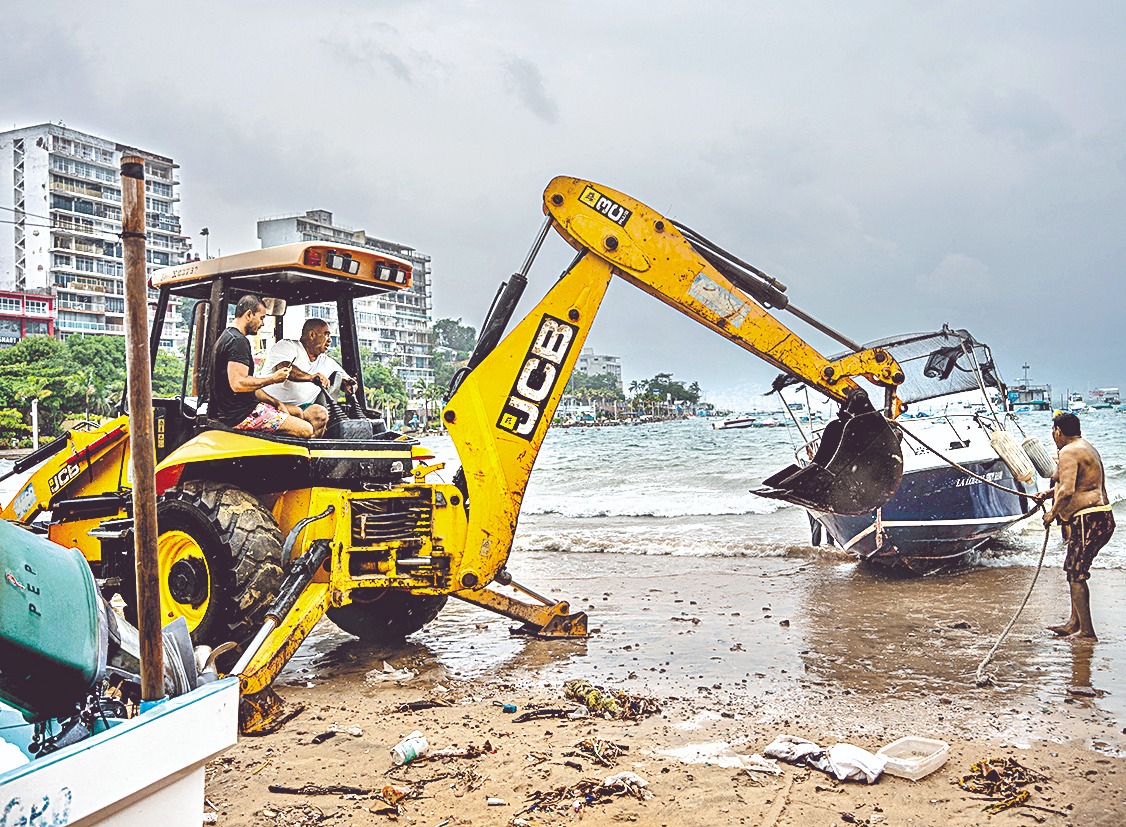 Personas retiran del mar una embarcación ante los riesgos del fenómeno en Acapulco. EFE