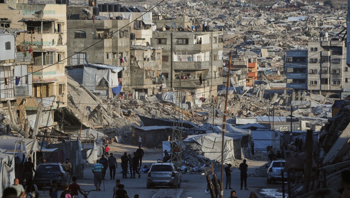 Palestinos caminan por una calle rodeada de edificios destruidos en los ataques israelíes | Foto: AP
