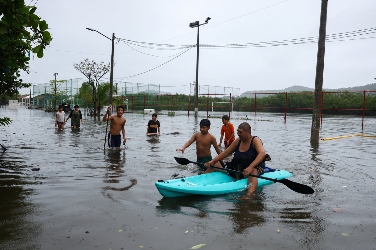 Personas atraviesan una calle inundada mientras el huracán Simon se acerca a la costa del Pacífico de México. | Reuters