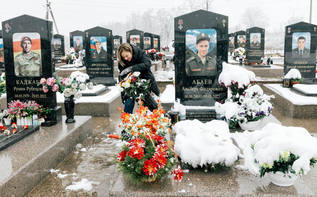Oksana Abaeva retira la nieve de las flores en la tumba de su hijo, Albert Abaev, en Vladikavkaz, capital de Osetia del Norte. | Nanna Heitmann/ NYT